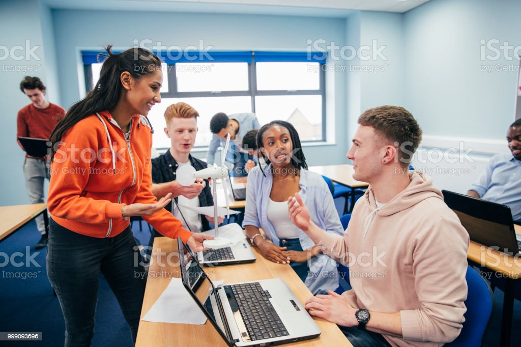 Una giovane donna mostra ai suoi compagni di classe un modello 3D di una turbina eolica durante la lezione di ingegneria. Entrambi gli studenti utilizzano un laptop.